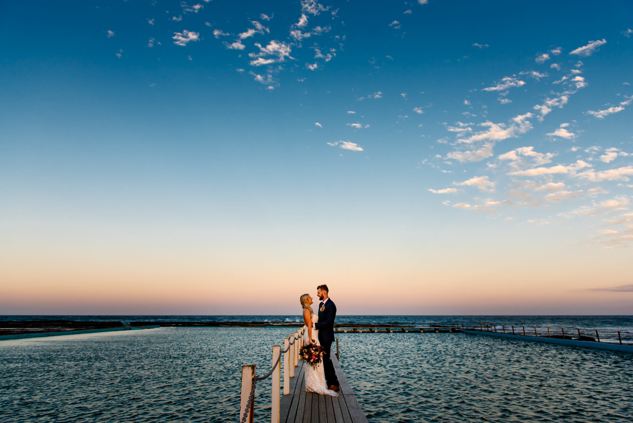 Newlyweds on dock at Narrabeen ocean pool at sunset