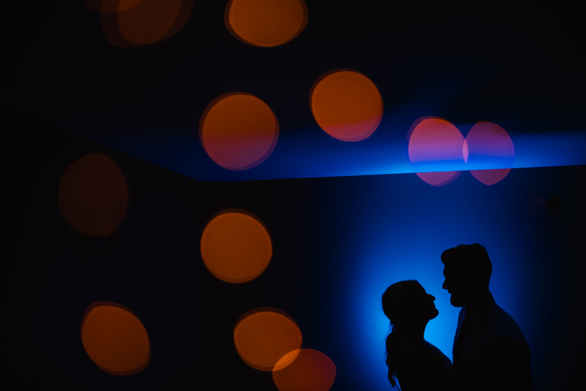 Silhouette of couple against a blue backdrop and golden lights in the background