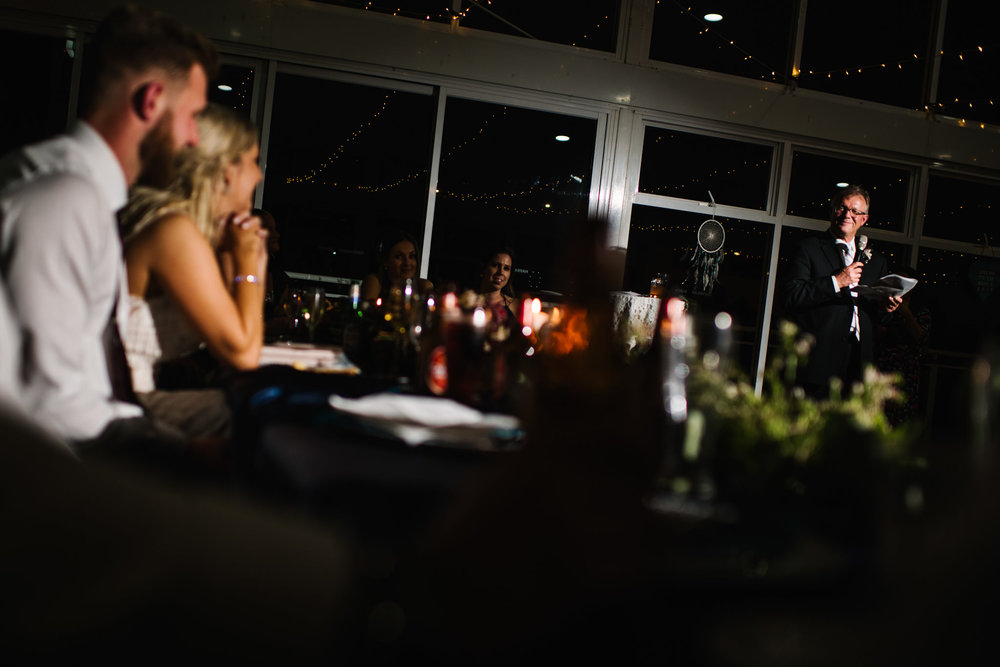 Newlyweds looking on at father of the bride giving an emotional speech