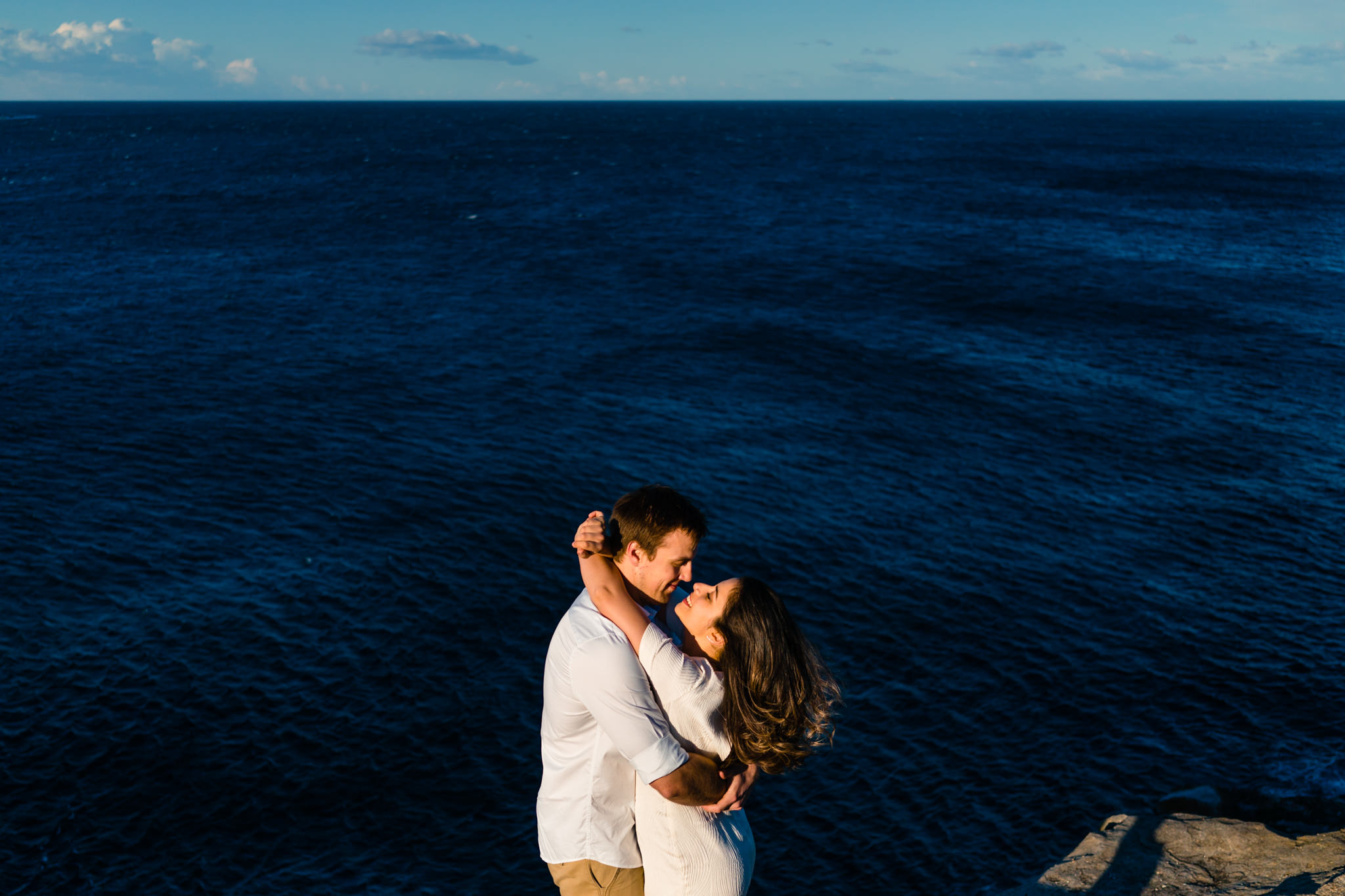 Couple kiss on cliff top with view of harbour in the backdrop