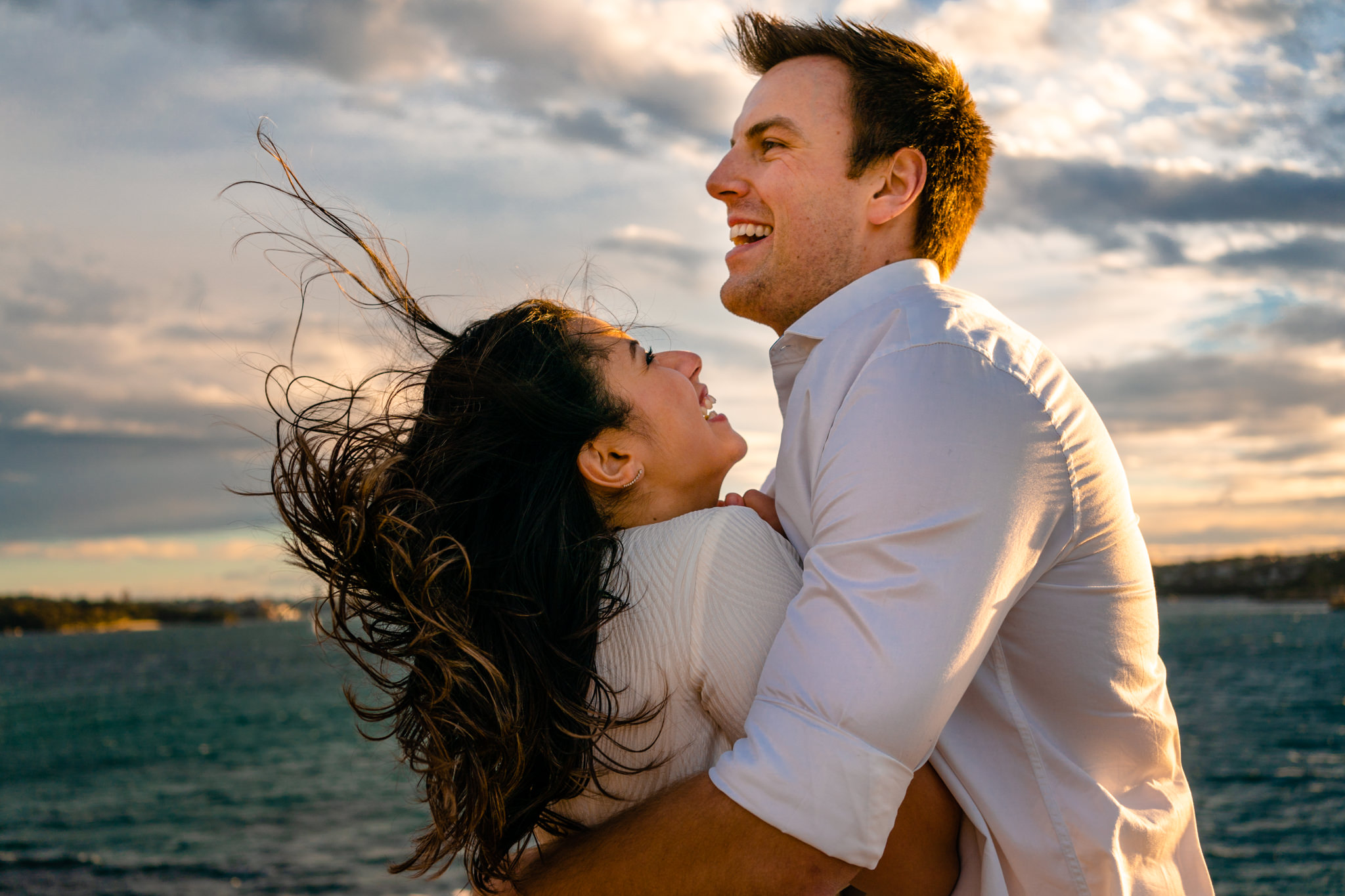 Couple laugh as wind blows their hair around during engagement session at Watsons Bay