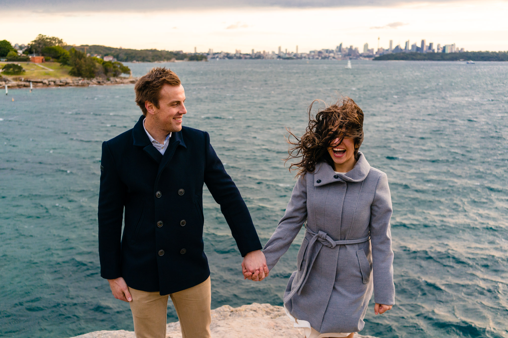 Couple laughing as wind blows during ocean front engagement session 