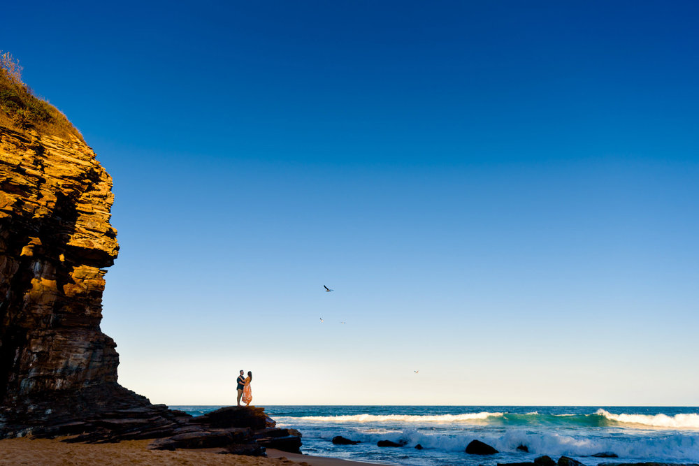Couple on rocks with ocean and cliff face in the background