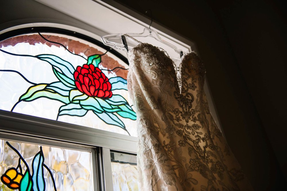 Bridal gown hangs in front of stained glass window