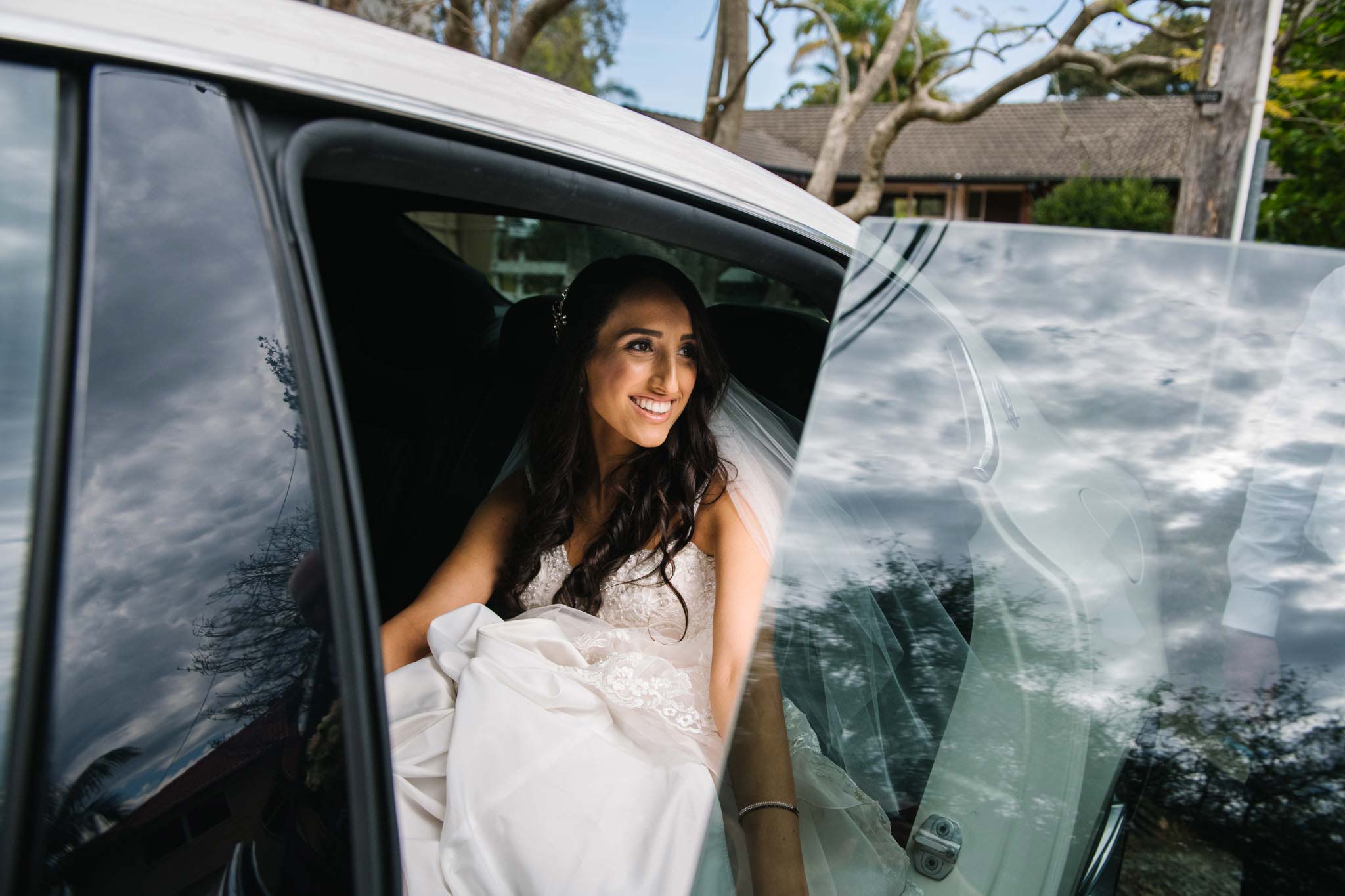 Bride smiling as she climbs into wedding car