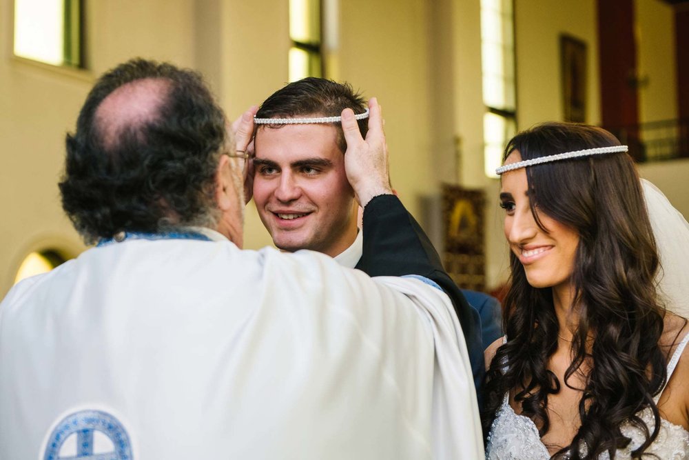 Priest puts crown on grooms head during Greek orthodox wedding ceremony in Sydney