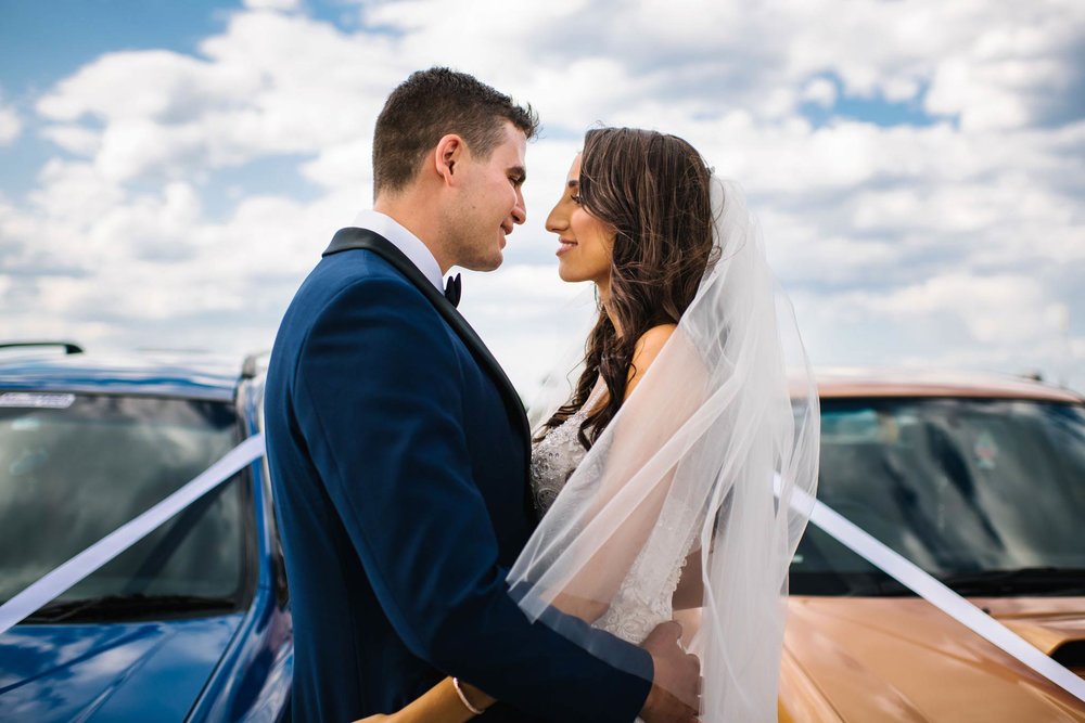 Newlyweds embracing in front of muscle wedding cars