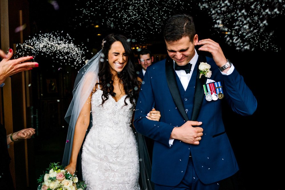 Bride and groom laugh as guests throw rice on them as they exit the church