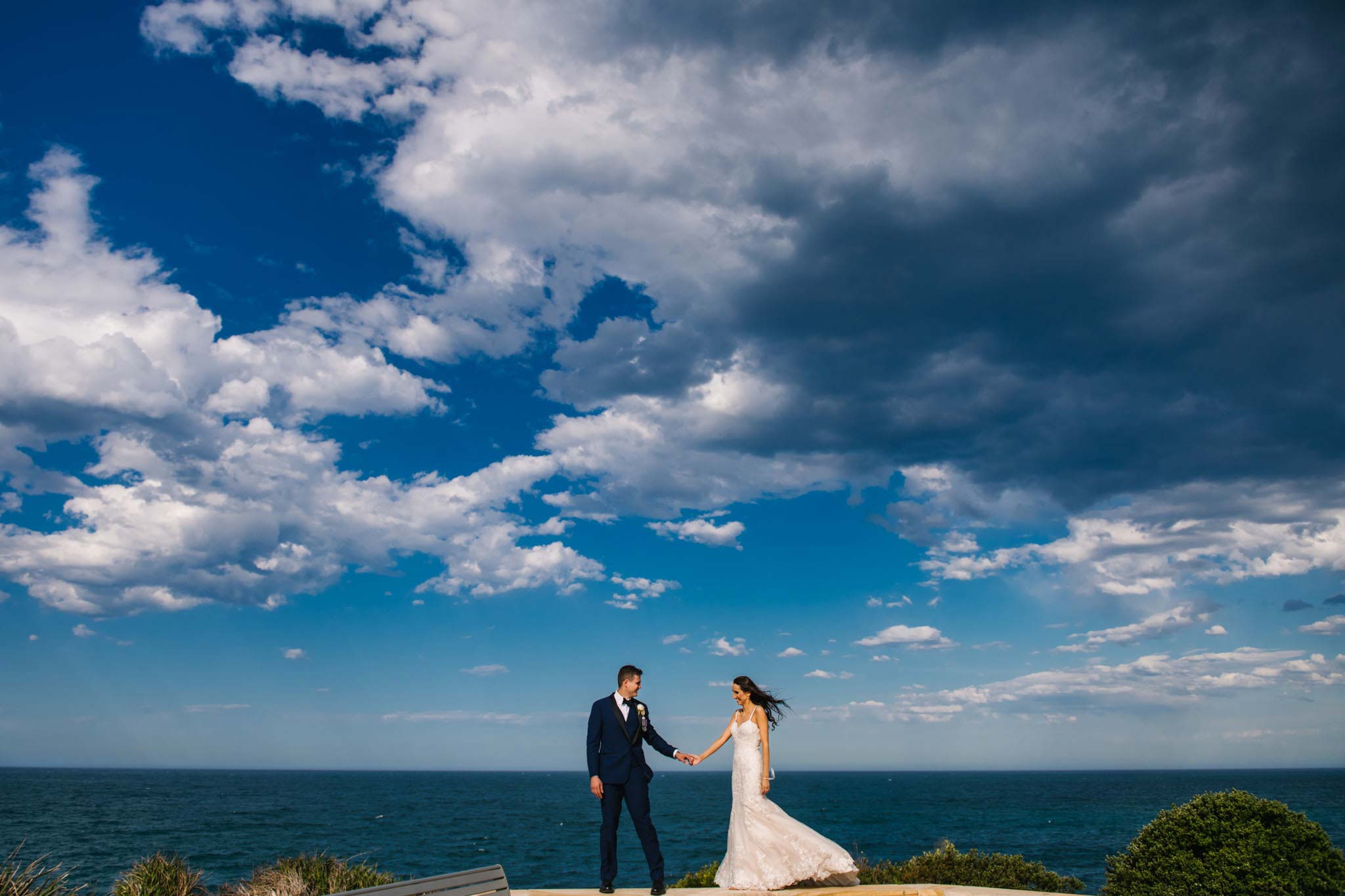 Beautiful view of the ocean at Freshwater headland with newlyweds walking along stone wall