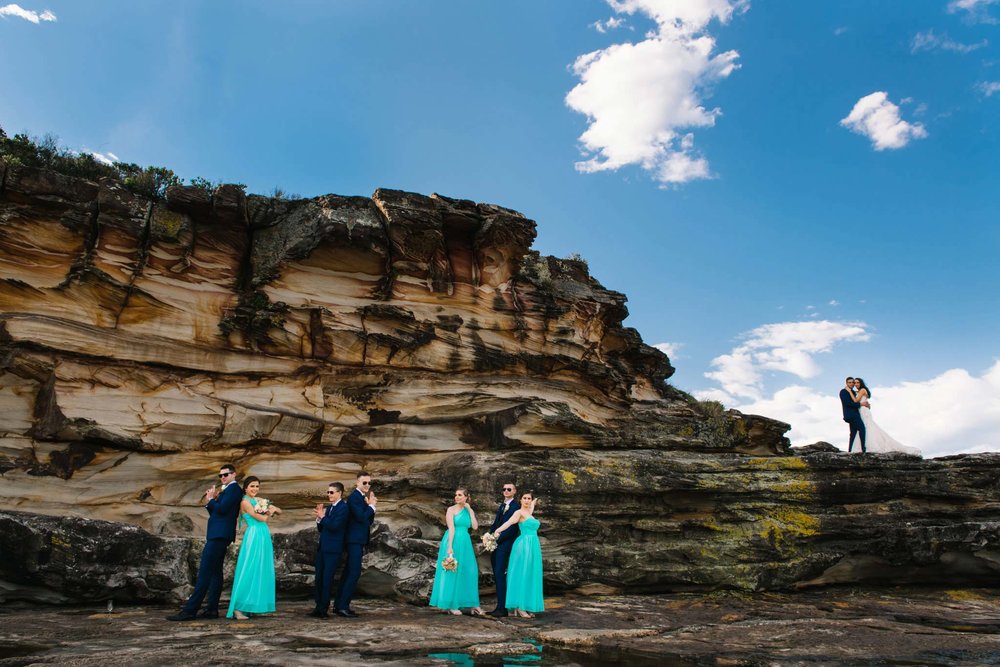 Bridal party in front of a sandstone cliff with newlyweds in the backdrop at Freshwater headland
