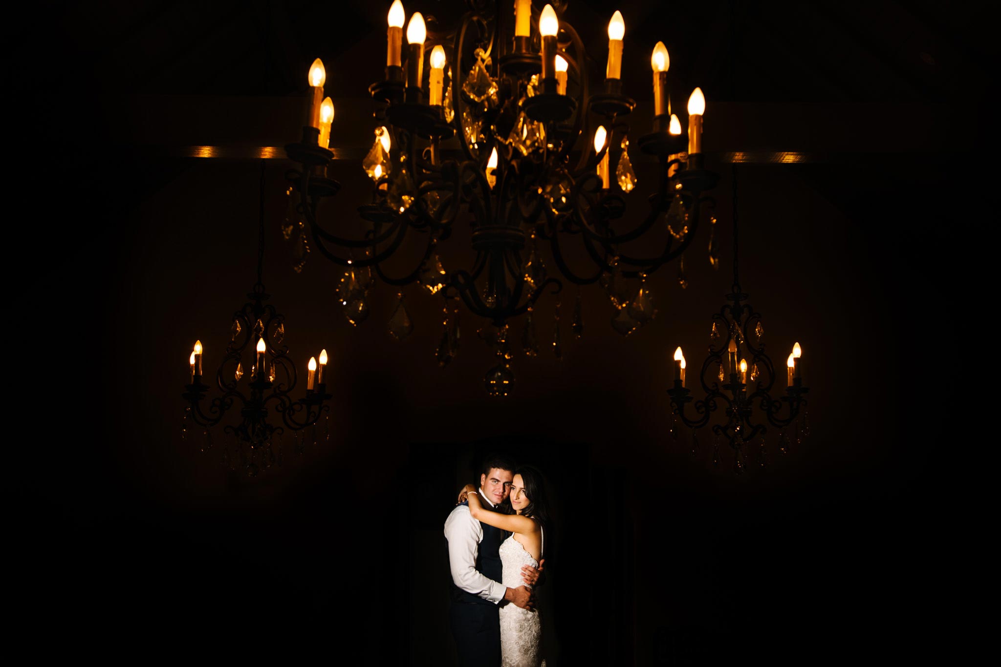 Bride and groom embrace under chandeliers at Manly Golf Club wedding reception