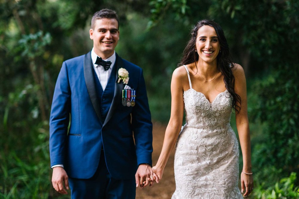 Groom and bride laughing as they walk through garden path at Manly Golf club