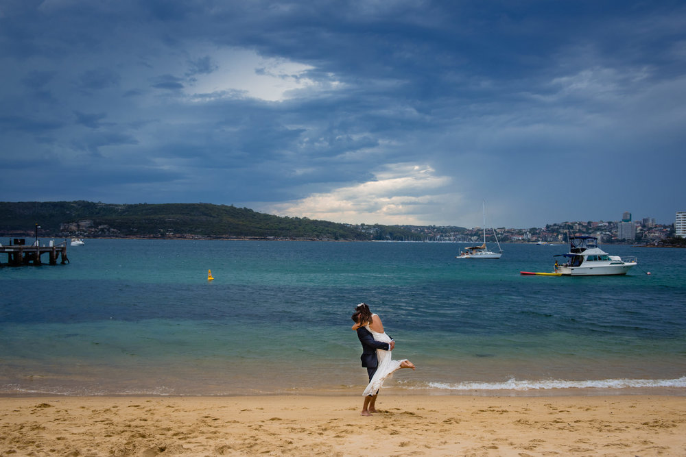 Newlywed couple embrace on beach at Q Station, Manly