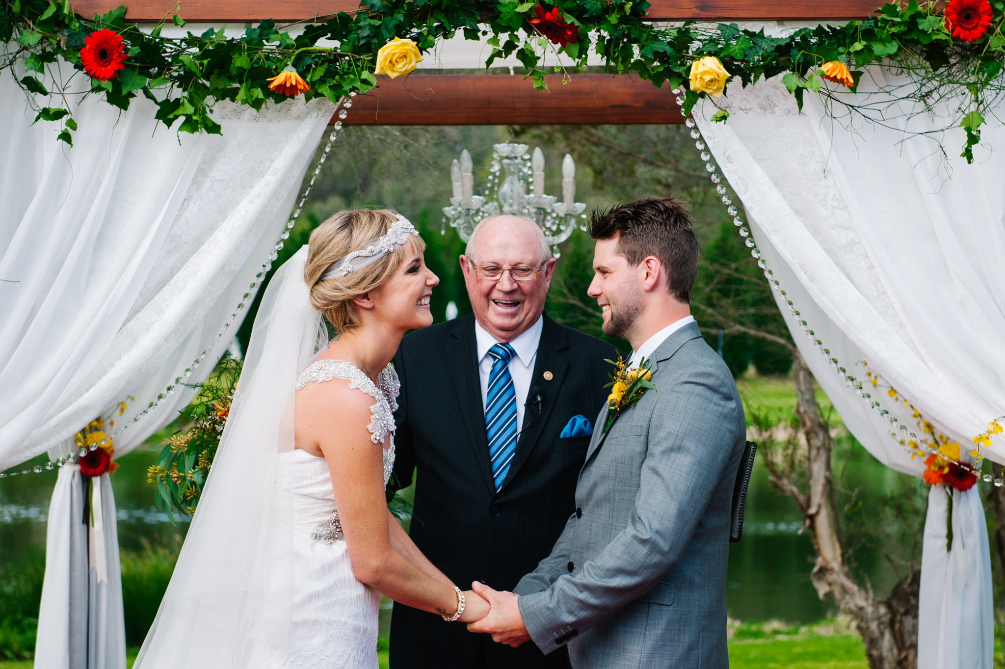 Bride and groom during ceremony under boho arbour at country wedding