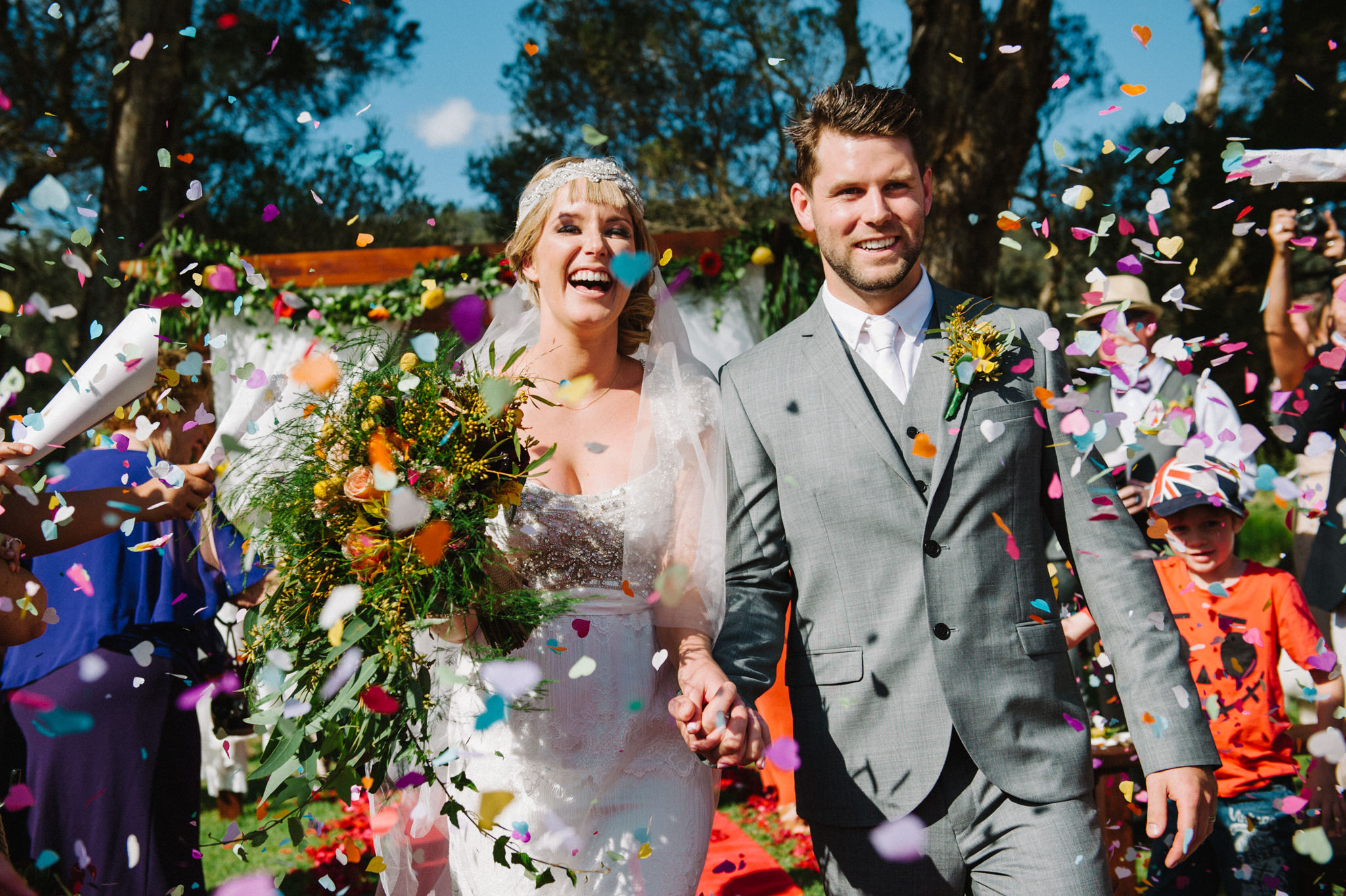 Happy newlyweds walking down aisle with rainbow confetti  