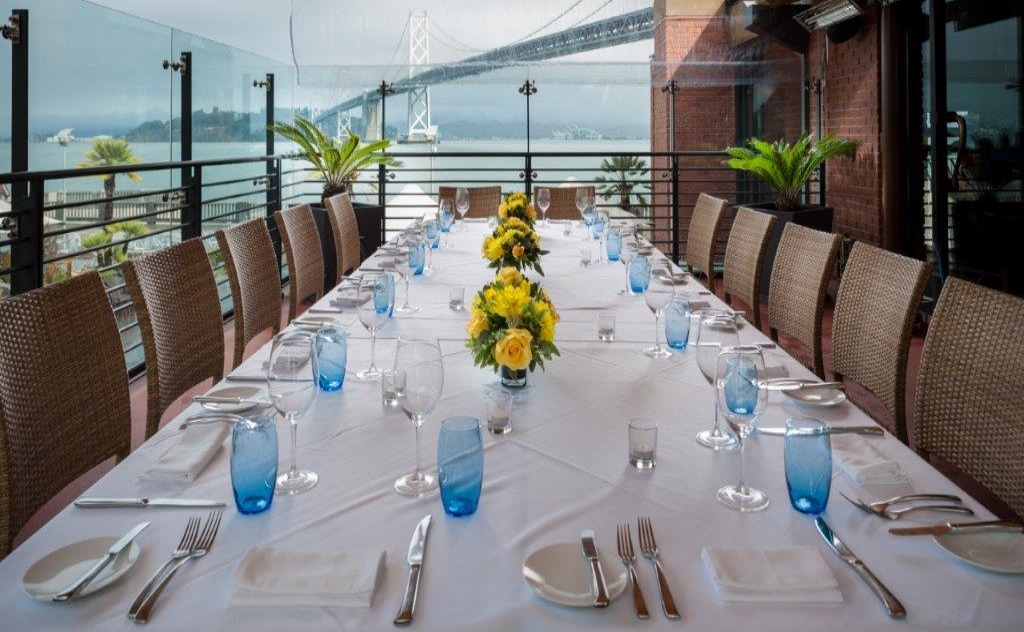 photo of detailed set up of long private dining table with view of Bay Bridge in the background.