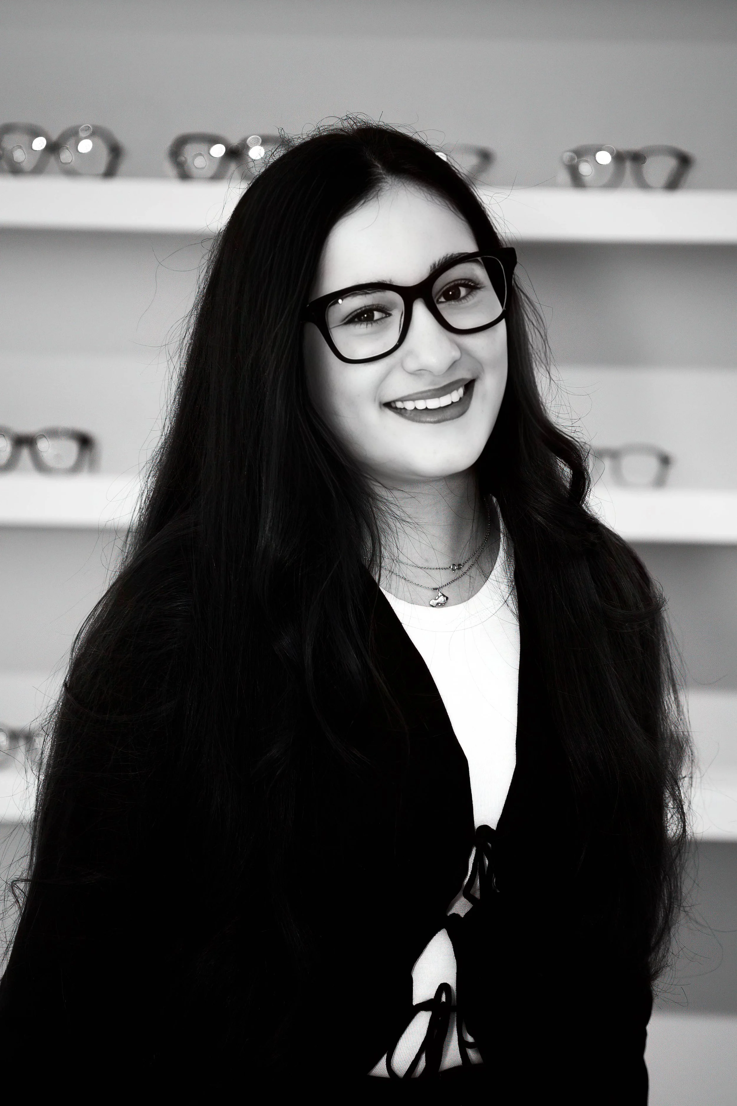 Portrait en noir et blanc d'une femme souriante portant des lunettes, avec des lunettes en arrière-plan.