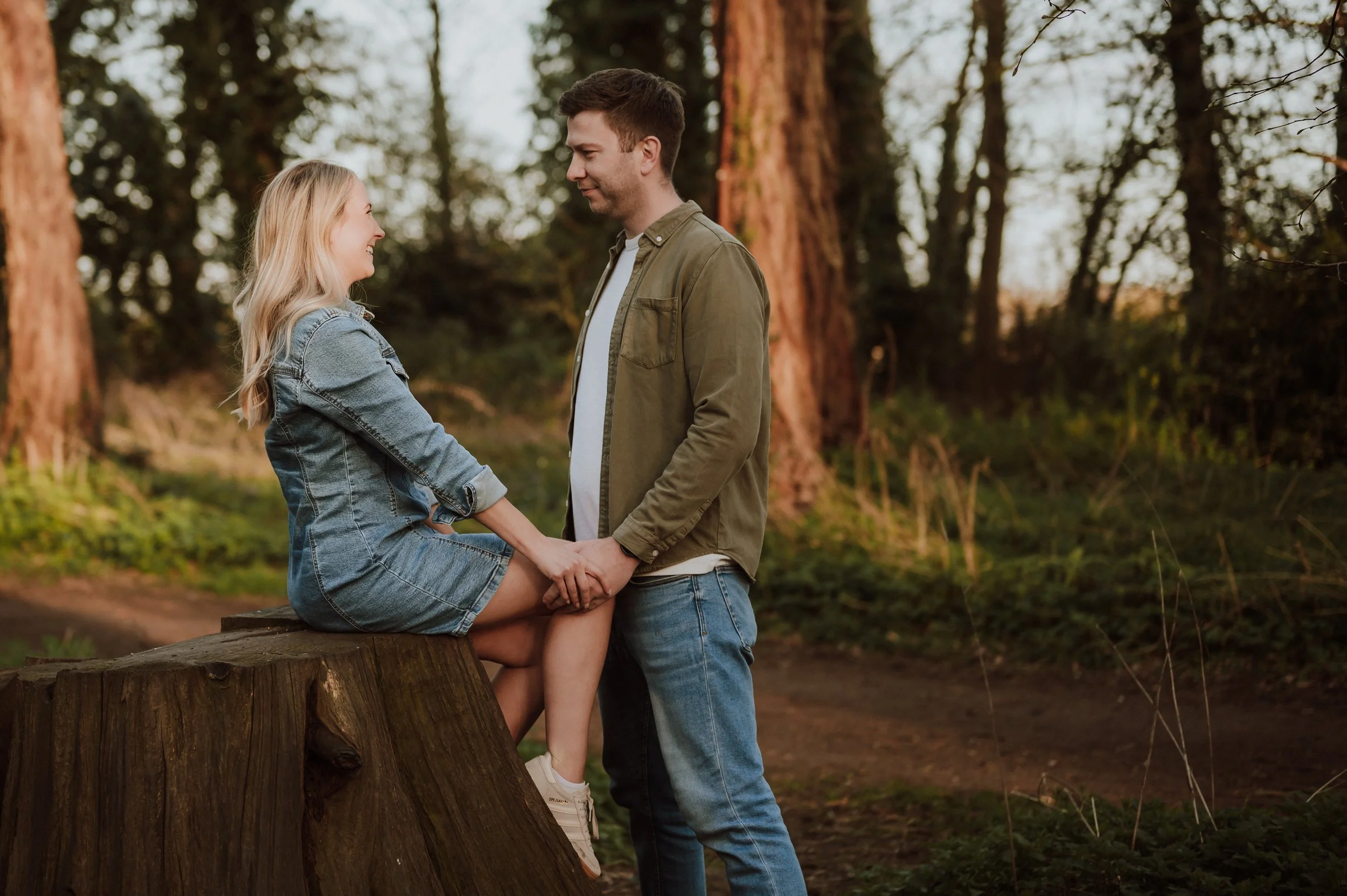A couple in love holding hands and looking at each other in a forested area during sunset.