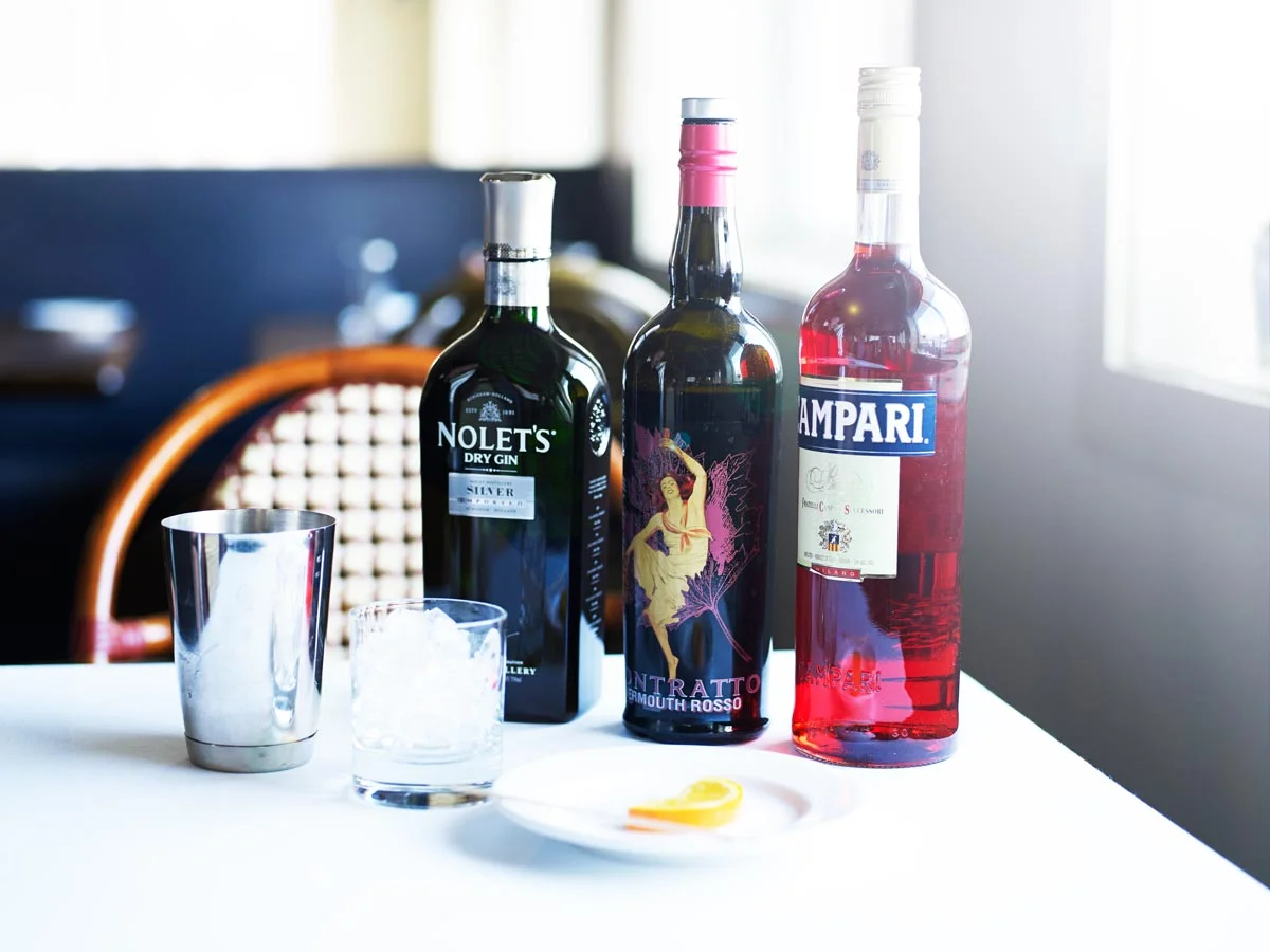 Three bottles of alcohol, a glass with ice, and a metal cup on a table.