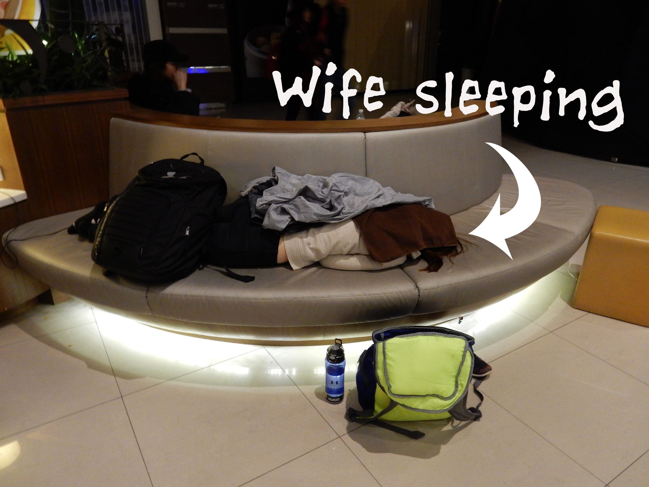 Wife pretending to be a pile of clothes as she sleeps at Taipei International Airport