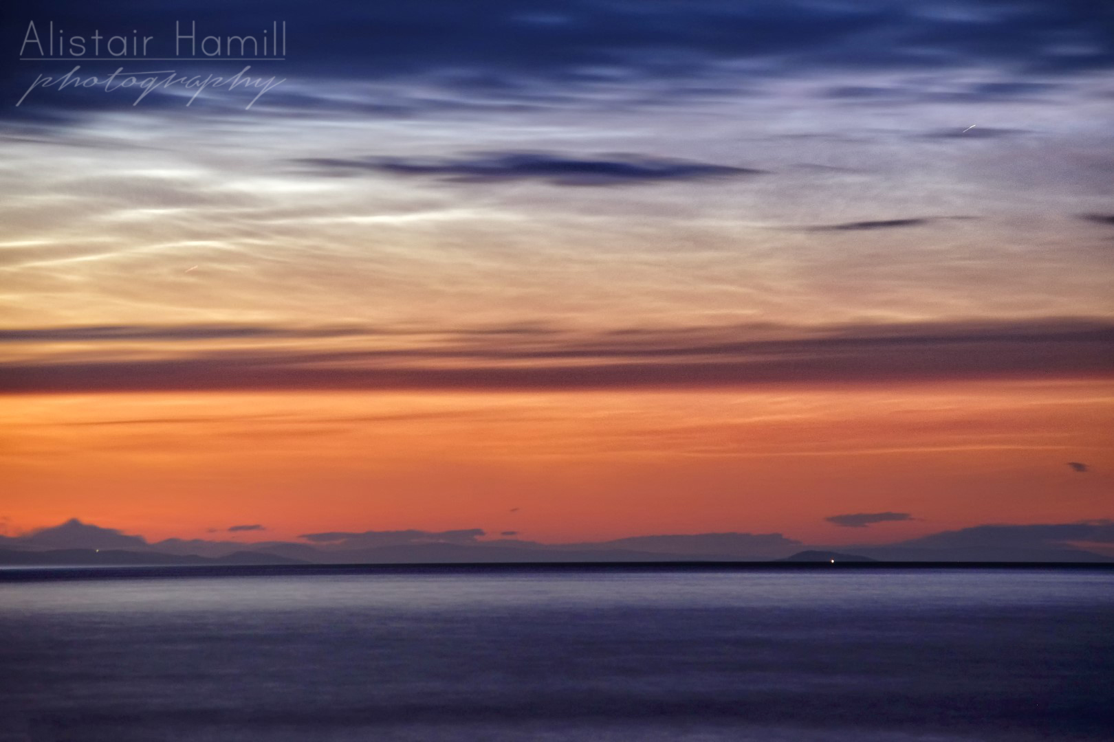 The lighthouse at Sanda Island shines all the way over to Garron Point, while the noctilucent clouds put on a wonderful display in the skies above. 