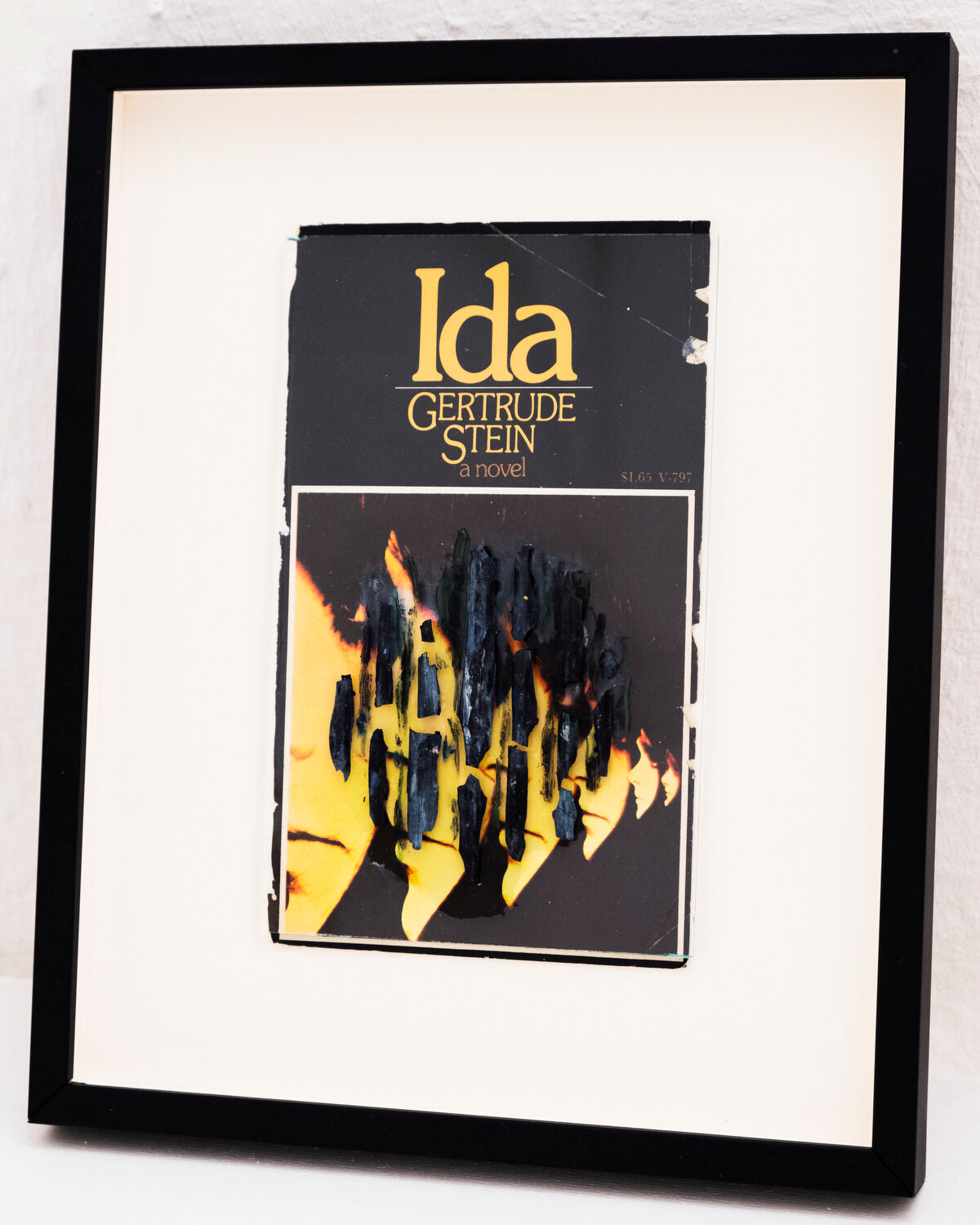   Ida , 2019 After Gertrude Stein ‘ Ida ’ Book cover, flakes of paint, oil on glass image: 18 x 11,5 cm ; 7 1/8 x 4 1/2 in frame: 27,5 x 22,5 x 2,5 cm ; 10 7/8 x 8 7/8 x 1 in   photo Jean Marques  