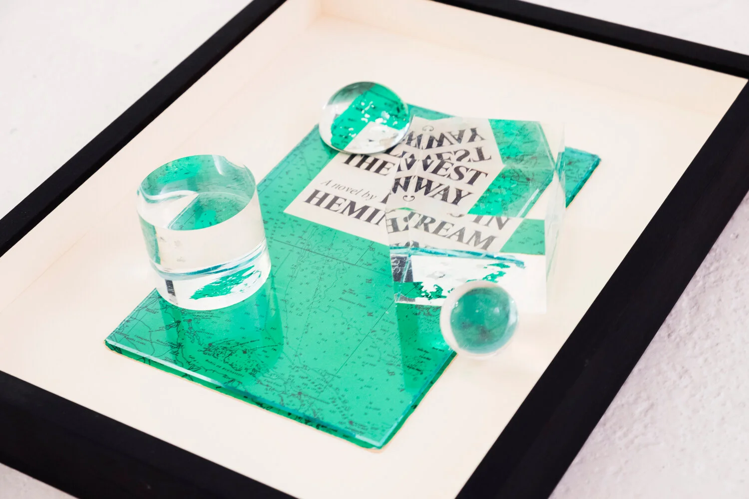  Islands , 2019 After Ernest Hemingway ‘ Islands in the Stream ’ Book cover, glass, Plexiglas shapes, acrylic sphere image: 20 x 17 x 5,5 cm ; 7 7/8 x 6 3/4 x 2 1/4 in frame: 33 x 26,5 x 6,5 cm ; 13 x 10 1/2 x 2 5/8 in   photo Jean Marques  