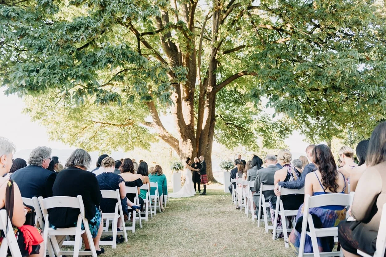 Bride and groom standing at end of aisle under a tree
