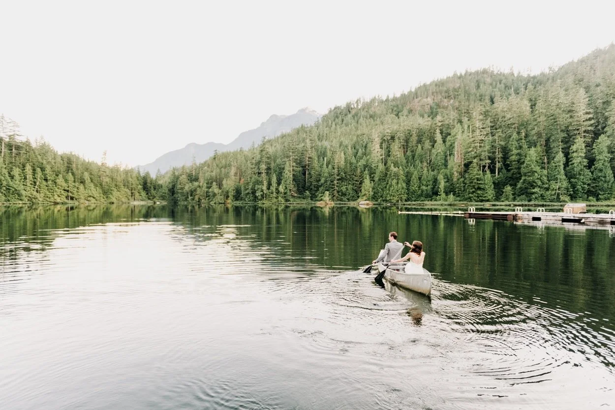 Bride and groom rowing canoe on lake surrounded by trees