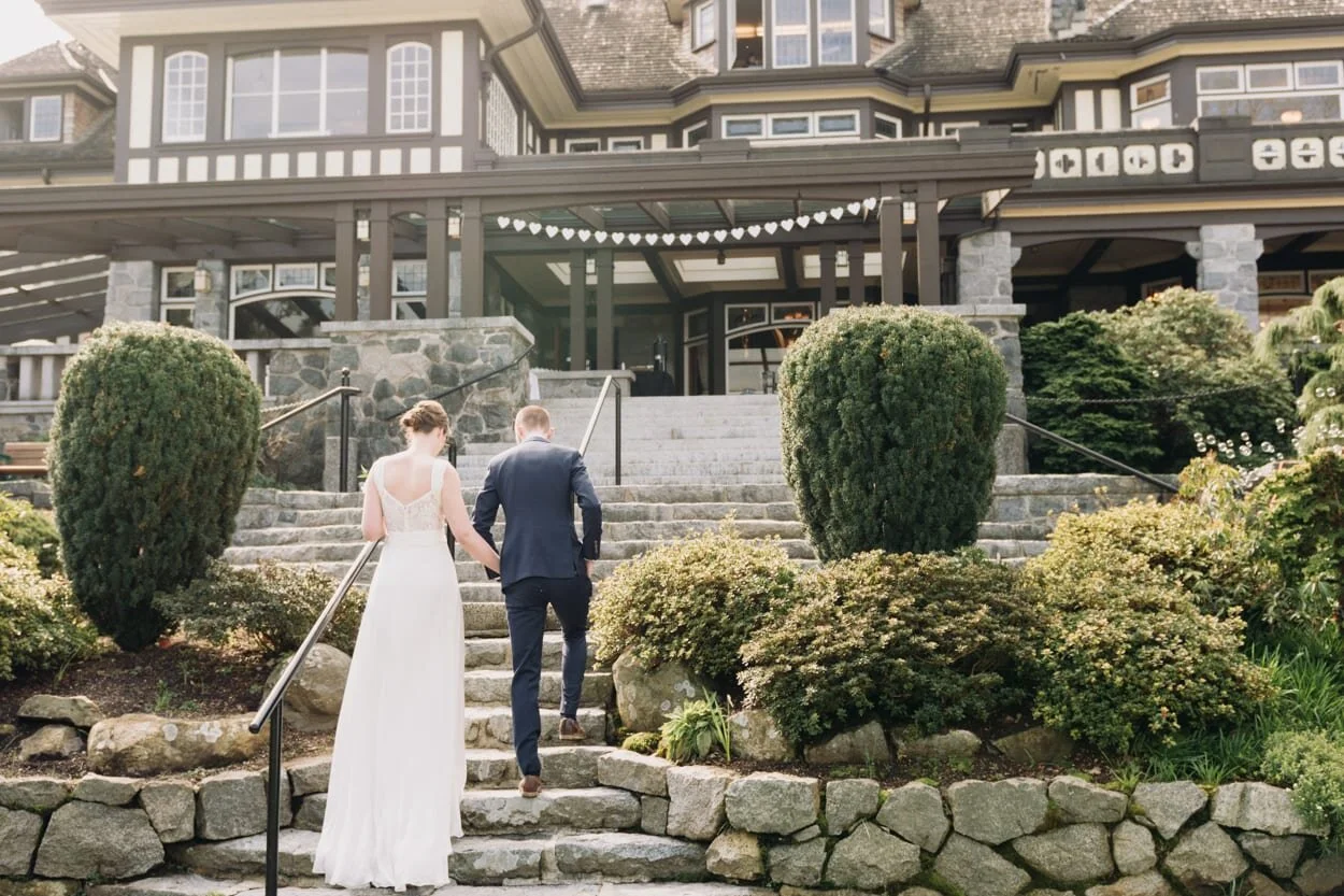 Bride and groom holding hands walking up stairs of large house