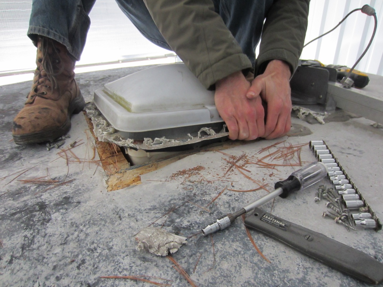 After removing the caulk from the screws and unscrewing the screw, we had to cut the rubber around the vents and then physically pull the vents out of the roof. Turns out the rubber fabric was also stapled to the sides of the wood vent opening.