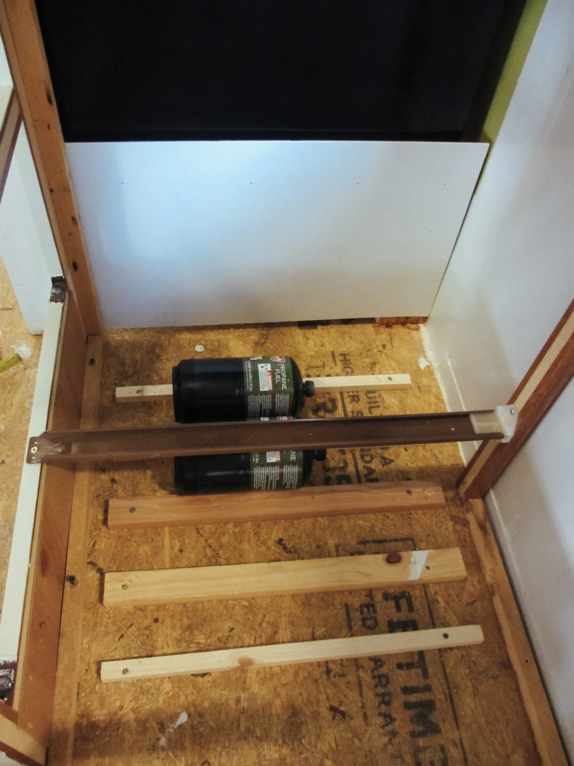 We installed pieces of wood under the RV stove/oven to hold the camping fuel bottles.