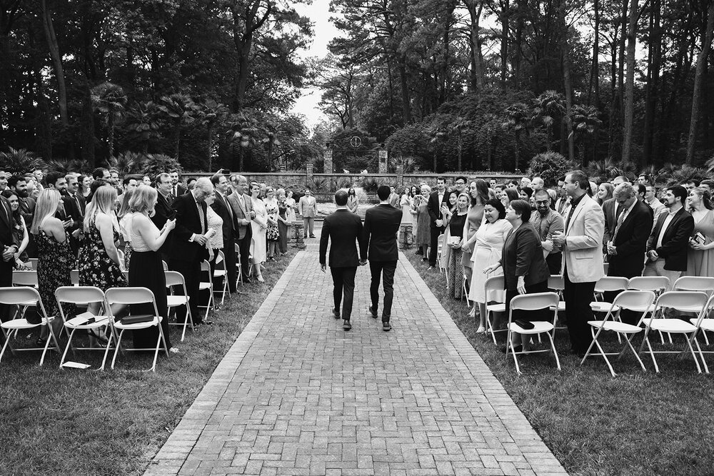  Two grooms walking down the aisle together. Vegan wedding at the Norfolk Botanical Gardens, Norfolk, VA. Rose garden and plant inspired wedding on the first day of Pride month. 