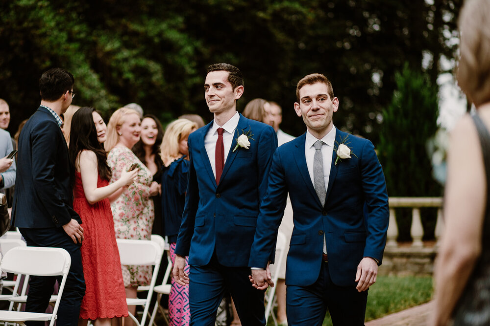  Two grooms walking down the aisle together. Vegan wedding at the Norfolk Botanical Gardens, Norfolk, VA. Rose garden and plant inspired wedding on the first day of Pride month. 