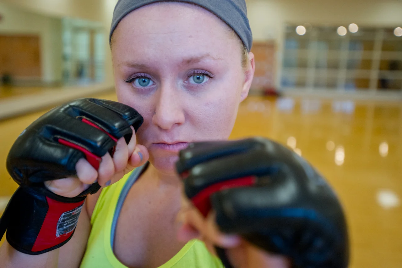 Jayde Sheeley poses for a portrait with her fighting gloves after her training session in the Ping Center in Athens, Ohio, on September 9, 2015. When asked about the intensity of the sport, Sheeley responds, "I kinda like getting black eyes. My dad told me before my first match that my face was probably gonna look like shit the next morning. But then I walked away with only one little bruise and I was like 'Seriously, I suffered through that match and got nothing?'" (©2015 Sarah Stier)