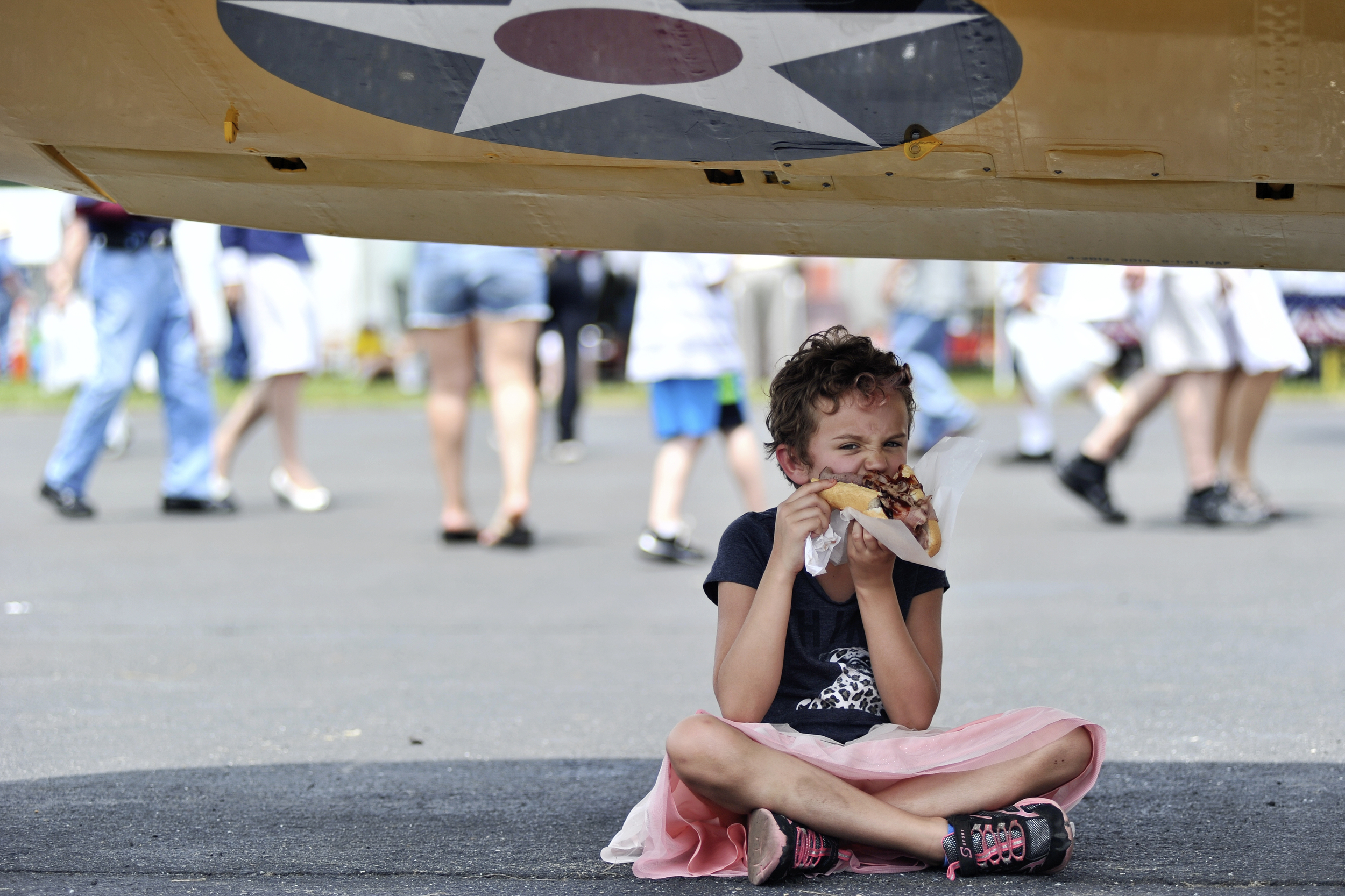 Addie Whitham, 8, of Philadelphia, PA, grabs a bite to eat under the shade of a plane wing at the World War II Weekend in Reading, PA, on June 4, 2016. (Reading Eagle: Sarah Stier)