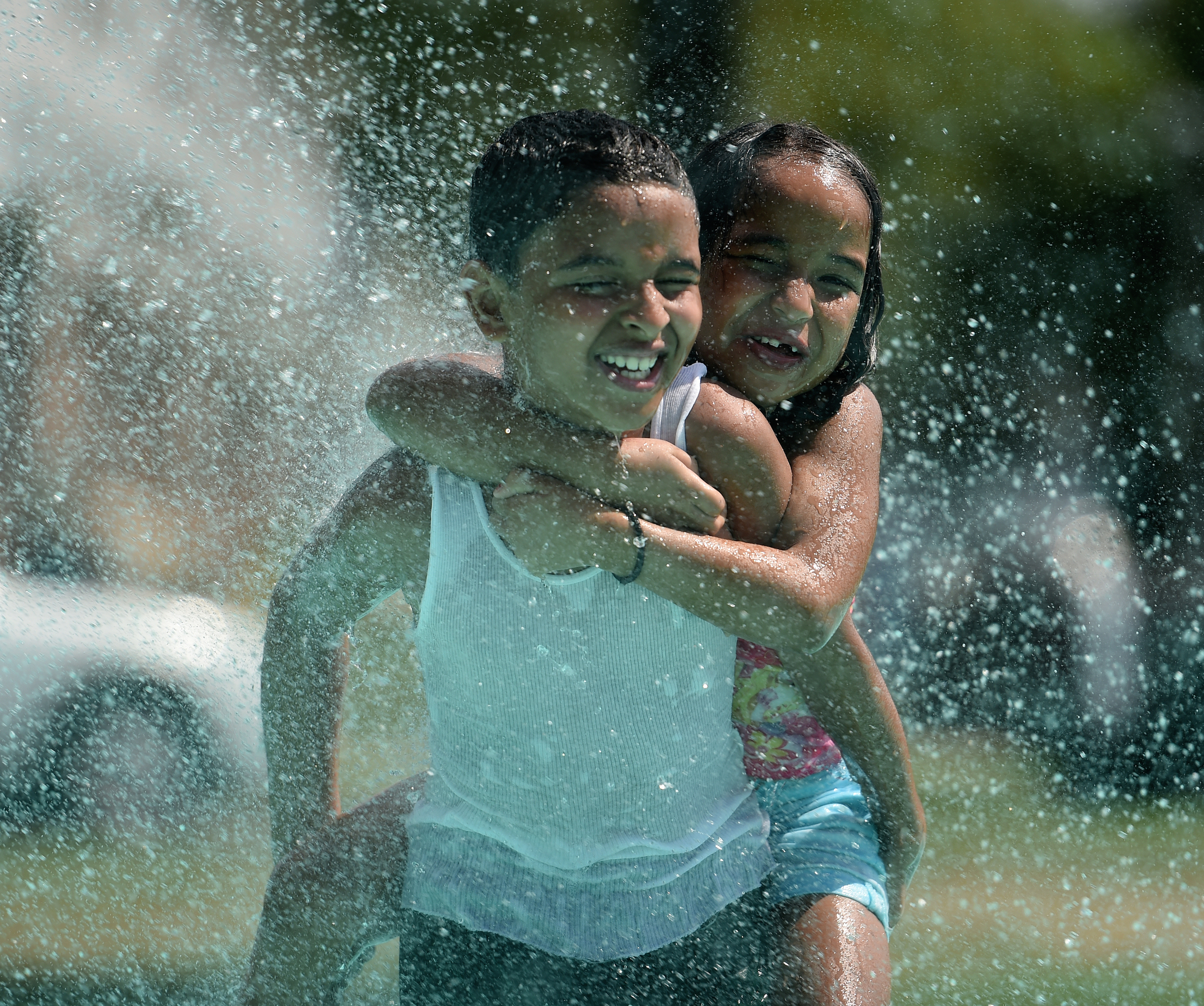 Noah Delvalle, 10, gives Leandra Tavarez, 7, of Reading a piggyback ride in the splash pad at Yarnell Park in Shillington, PA, on July 21, 2016. The temperature in Shillington that day reached 95 degrees. (Reading Eagle: Sarah Stier)
