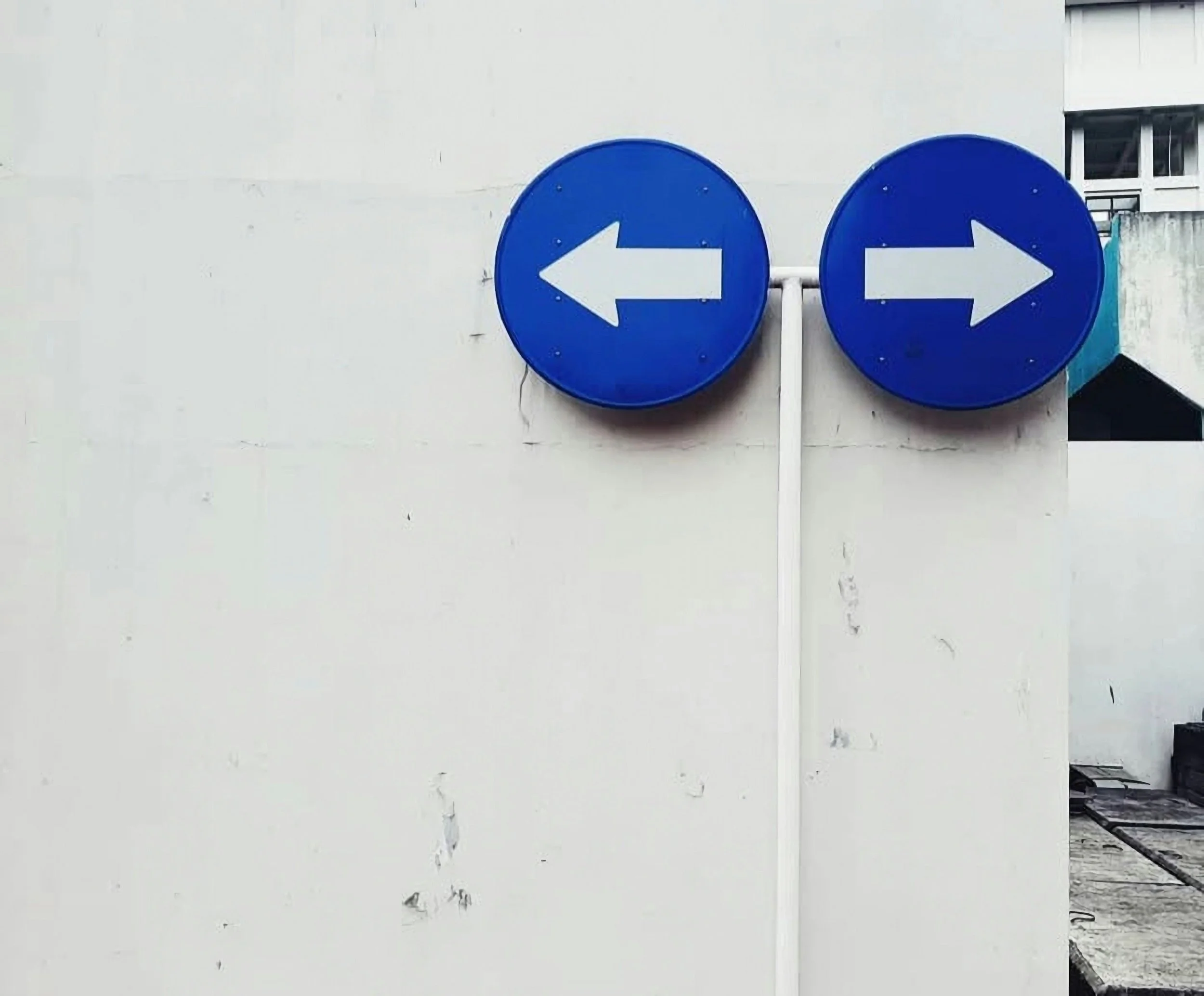 Two round blue signs with white arrows pointing left and right against a white wall.