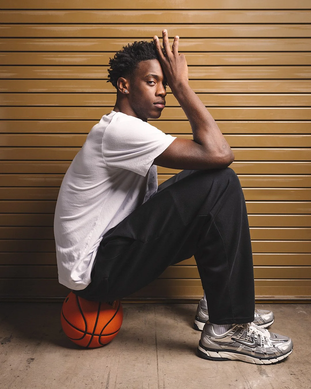  Editorial portrait of BYU basketball star AJ Dybantsa for a Sports Illustrated cover feature. Dybantsa, a top 2026 NBA Draft prospect, sits on a basketball in a minimalist studio, wearing BYU Cougars gear and silver sneakers. Photographed by MANICPR