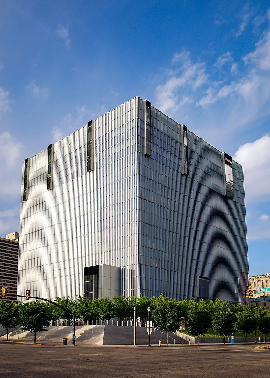  Exterior architectural photography of the SLC Courthouse in Salt Lake City. A high-angle view showcasing the building's geometric glass facade and vertical silver fins against a crisp blue sky, captured in the signature high-contrast style of MANICP