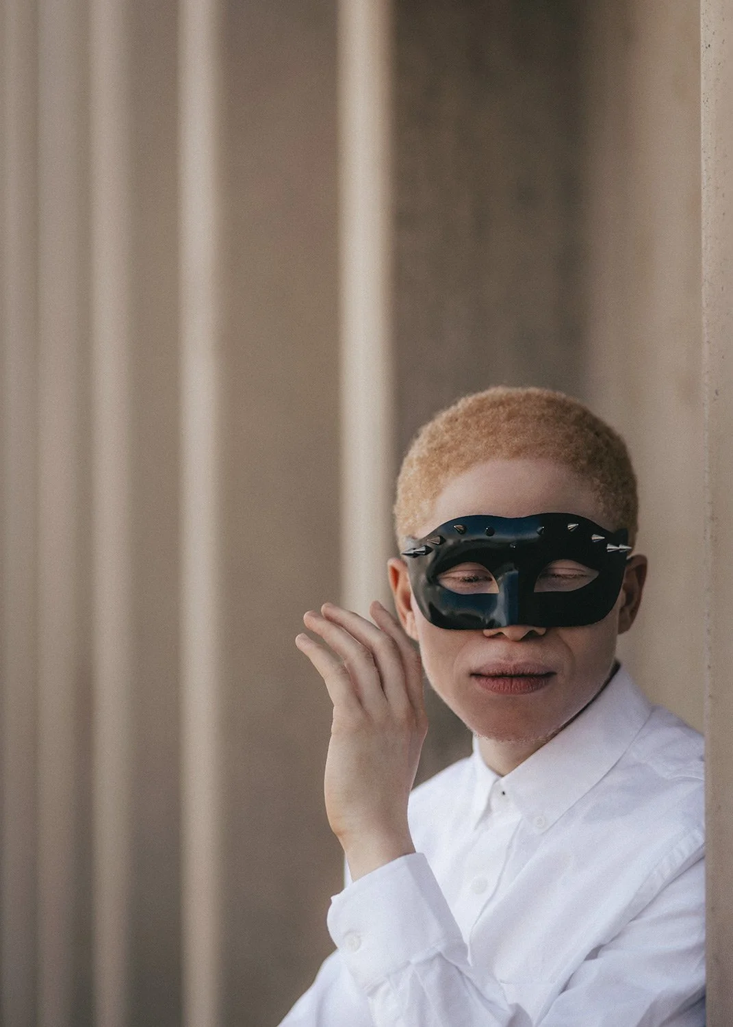  High-contrast studio portrait of a young albino man with very short blond hair, wearing a black masquerade mask and a crisp white button-up shirt. Photographed by MANICPROJECT in Salt Lake City, this cinematic and conceptual editorial image highligh