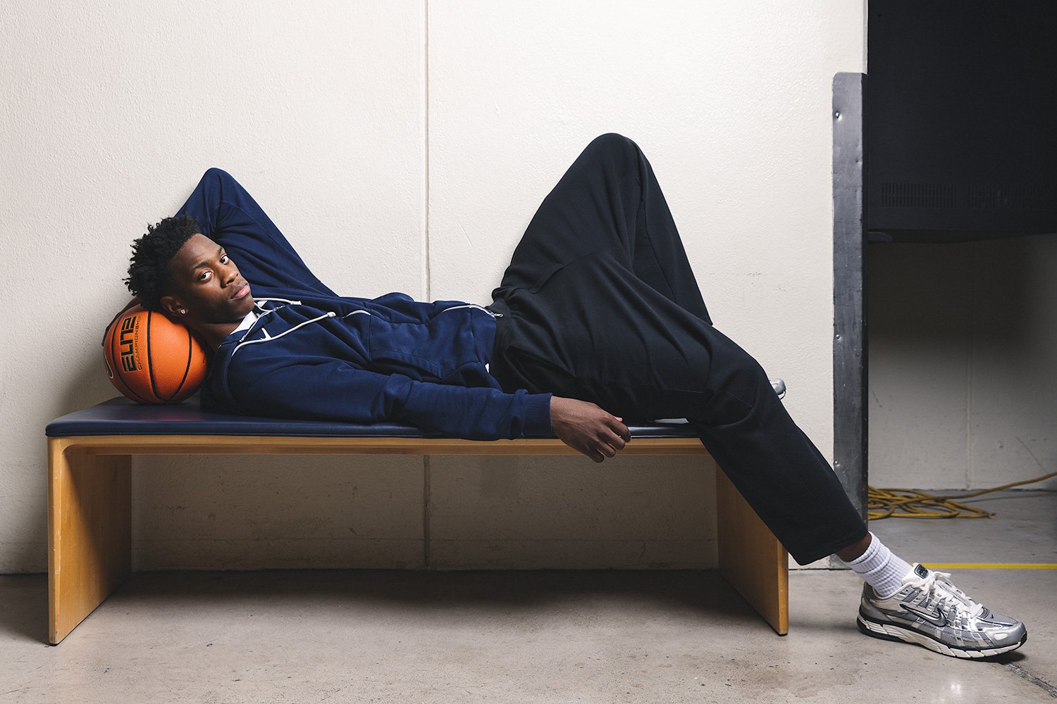 Professional portrait of BYU basketball star AJ Dybantsa lying on a locker room bench, holding a basketball behind his head, photographed for Sports Illustrated by MANICPROJECT