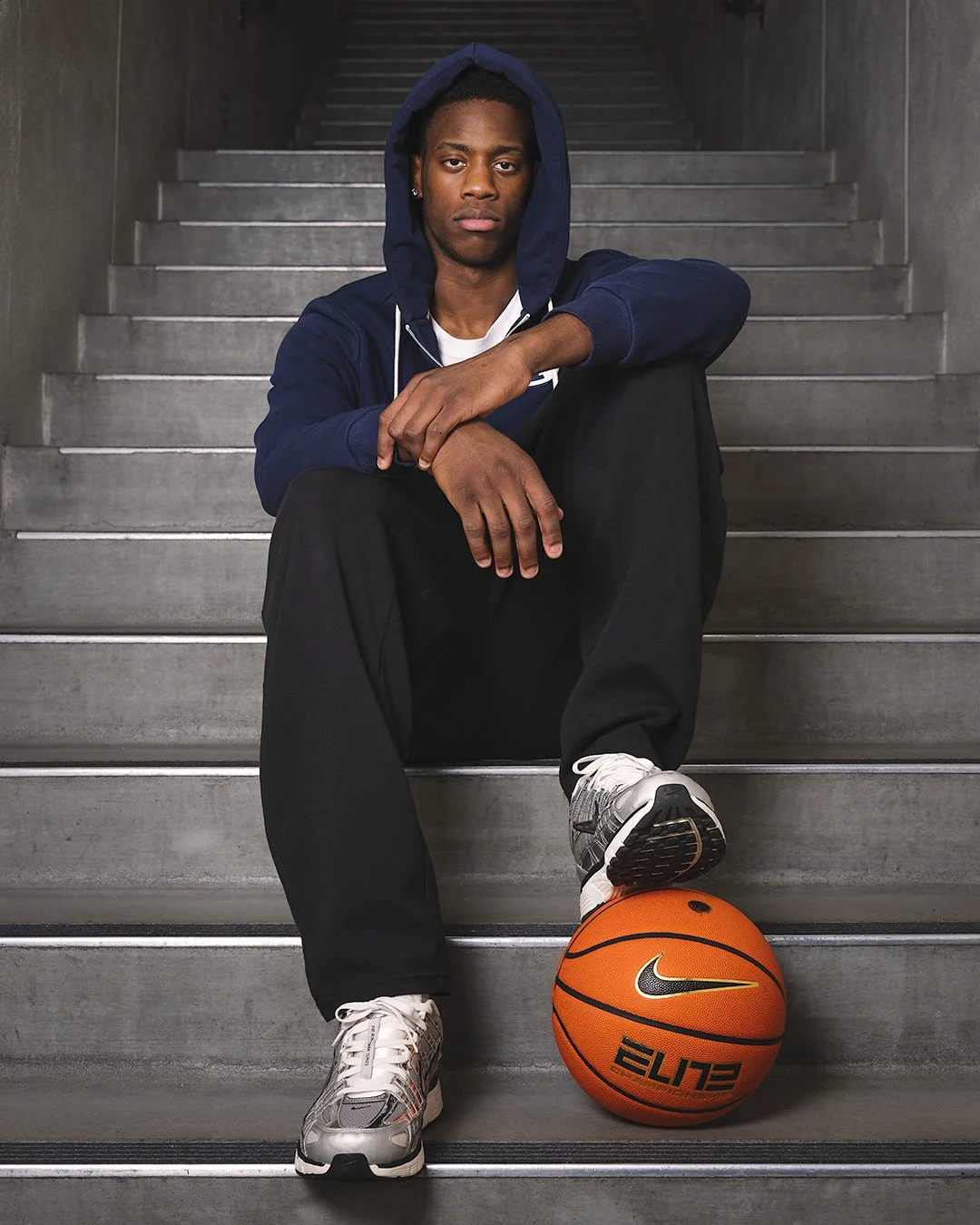 Editorial portrait of AJ Dybantsa sitting on concrete stairs with a basketball for Sports Illustrated. Magazine-worthy studio photography by MANICPROJECT, capturing the presence and athletic scale of the top NBA prospect