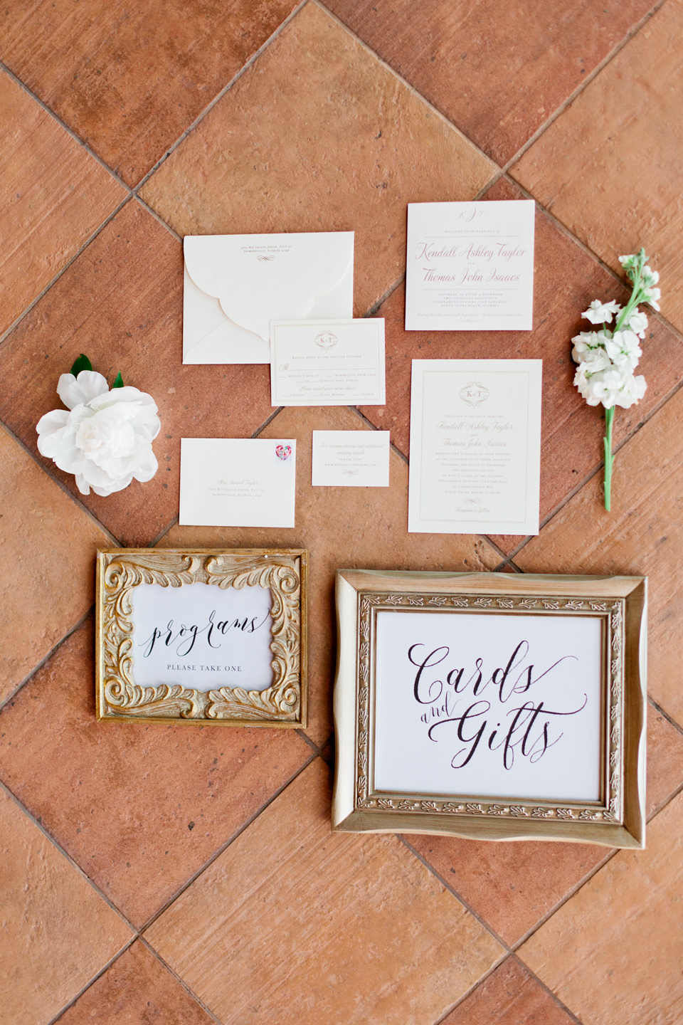 Picture of a wedding stationary suite with hand lettered signage and floral accents.  These are laying on terracotta tile flooring at the TPC Sawgrass in Ponte Vedra, Florida