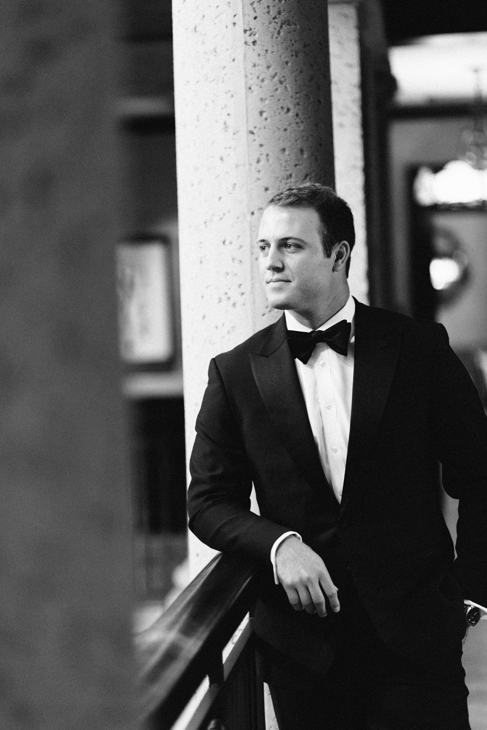 Image of a black and white portrait of a groom on his wedding day.  The groom is wearing a black tuxedo and leaning on the railing at the TPC Sawgrass in Ponte Vedra, Florida