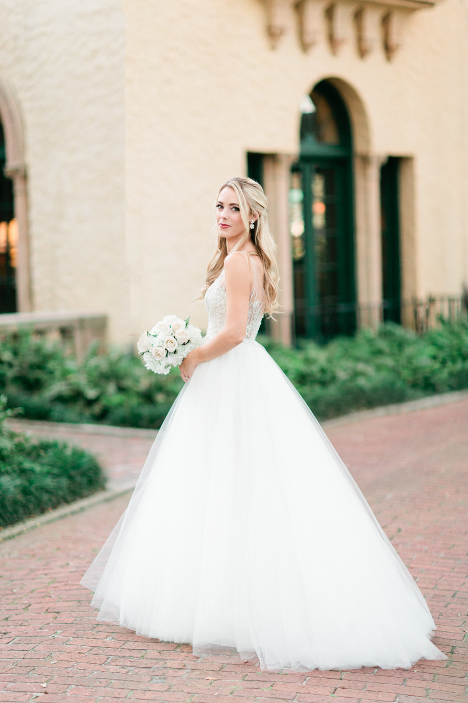 Image of a bride in a wedding gown in front of the Epping Forest Yacht Club in Jacksonville, Florida.  She is wearing a gown from Calvet Couture and holding a white bouquet.