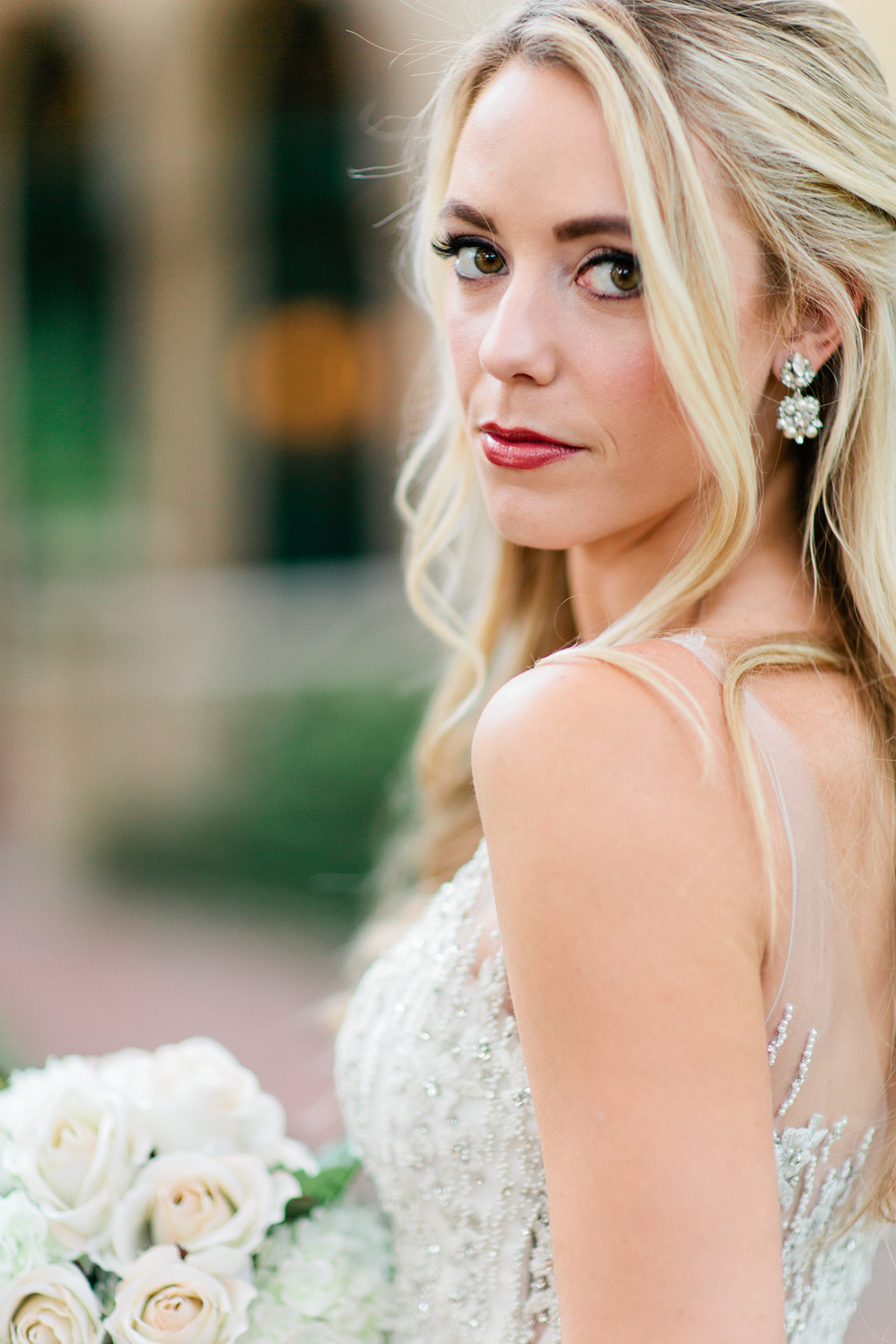 Image of a bride in a wedding gown, glancing over her shoulder.  Her hair is long and curled.  She is standing in front of the Epping Forest Yacht Club in Jacksonville, Florida