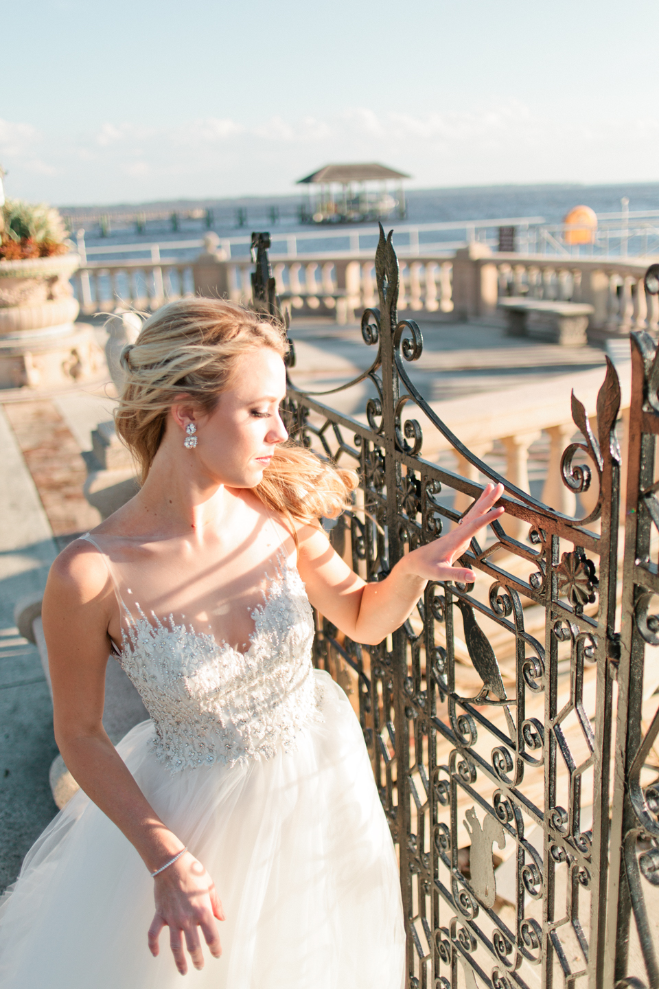 Image of a bride at an iron gate, looking out over the water in her Calvet Couture bridal gown.  The bride is at the Epping Forest Yacht Club in Jacksonville, Florida