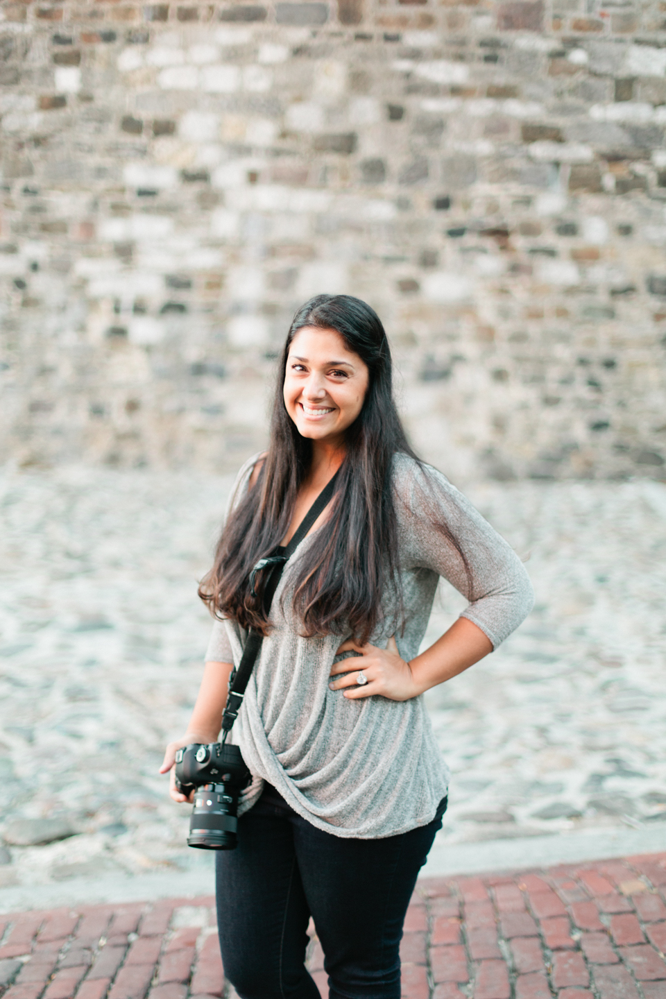 Picture of a female photographer in historic downtown Savannah, Georgia.  She is wearing a grey shirt, black pants, and is holding a Canon camera.  This is Rana of Roohi Photography.