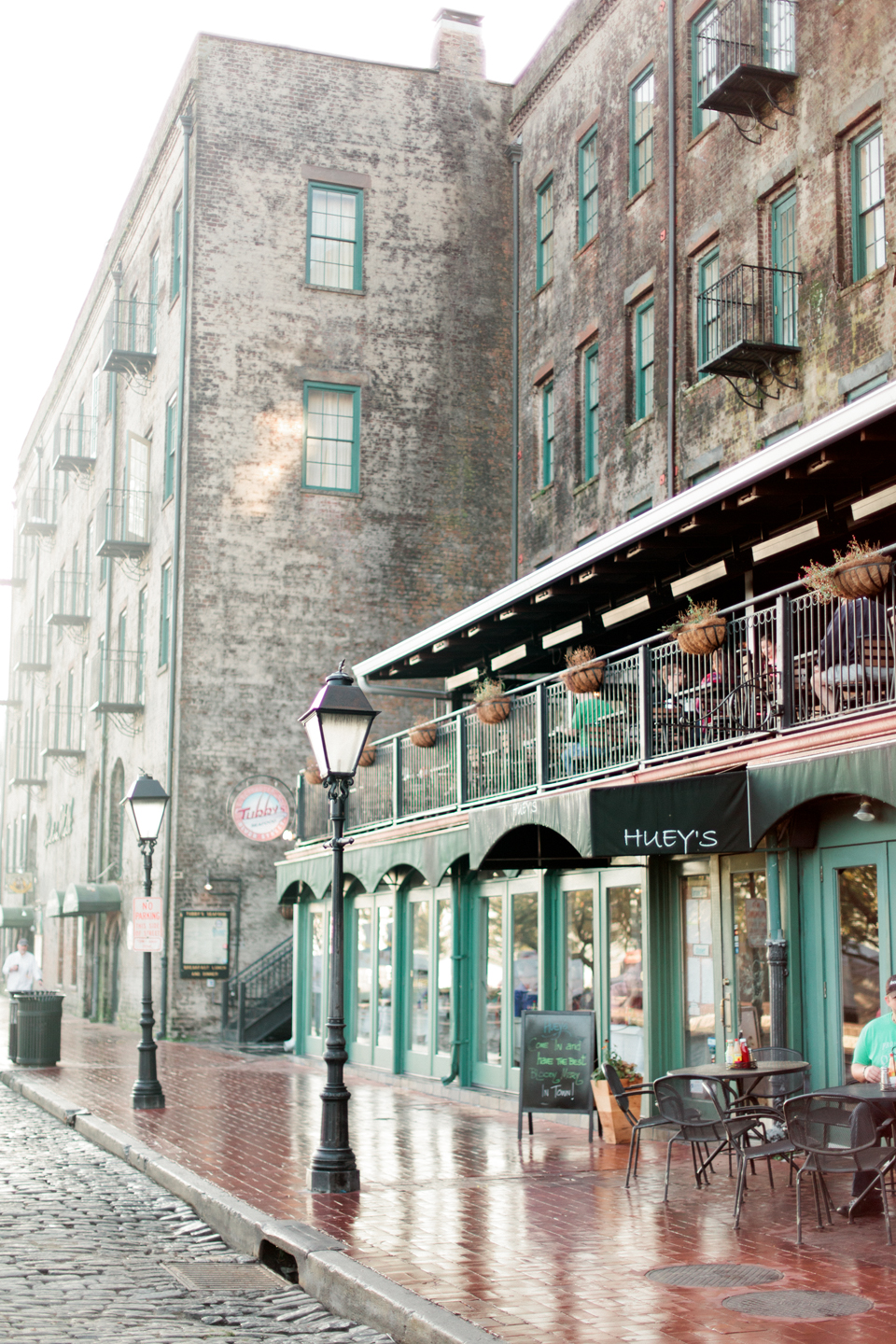 Image of East River Street in historic downtown Savannah.  There is a cobblestone street with a sidewalk cafe and lamp posts. 